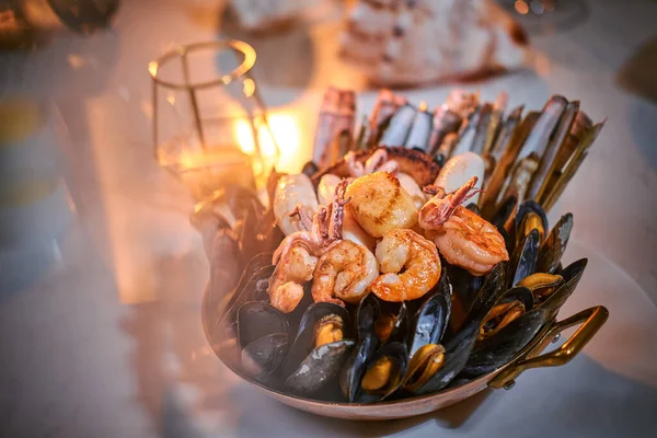 Eine Schüssel mit gegrillten Garnelen und Muscheln, serviert auf einem Steintisch neben goldener Kerze in einem Restaurant — Stockfoto