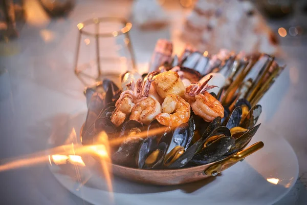 Eine Schüssel mit gegrillten Garnelen und Muscheln, serviert auf einem Steintisch neben goldener Kerze in einem Restaurant — Stockfoto