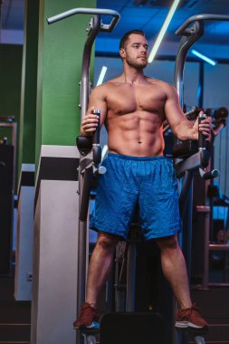 Strong bodybuilder standing on a parallel bars in a modern fitness center looking relaxed