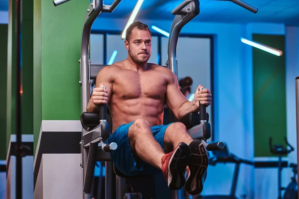 Strong bodybuilder doing excersise on a parallel bars in a modern fitness center — Stockfoto