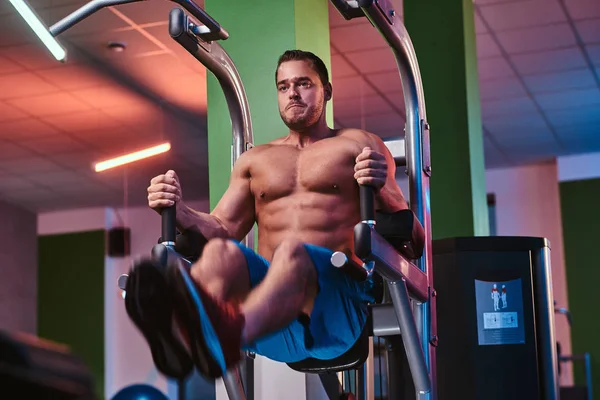 Strong bodybuilder doing excersise on a parallel bars in a modern fitness center — Stockfoto