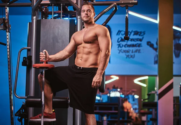Atleta posando sin camisa posando con una barra en un moderno y luminoso gimnasio — Foto de Stock