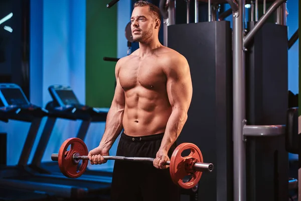 Hombre atlético con cuerpo muscular haciendo ejercicios con barra en un gimnasio — Foto de Stock