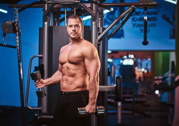 Athletic man with muscular body doing excersises with dumbbells in a gym — 스톡 사진
