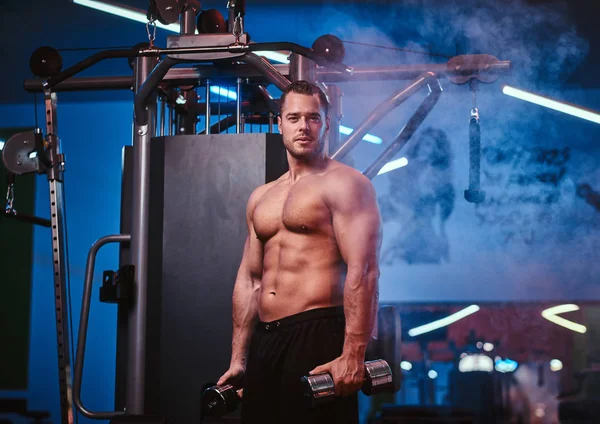 Homme athlétique avec le corps musculaire faisant des exercices avec des haltères dans une salle de gym — Photo