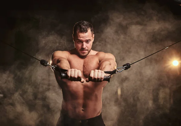 Спортсмен об'єднує руки, роблячи акведуки для своїх грудних м'язів у спортзалі, оточеному димом — стокове фото