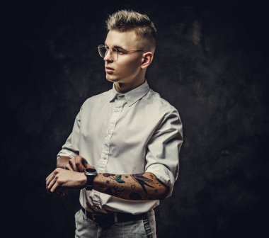 İddialı görünüşlü, ciddi görünen genç bir erkek öğrenci. Saatlerini stüdyoda takıyor. Gri bir arka planda izole edilmiş.