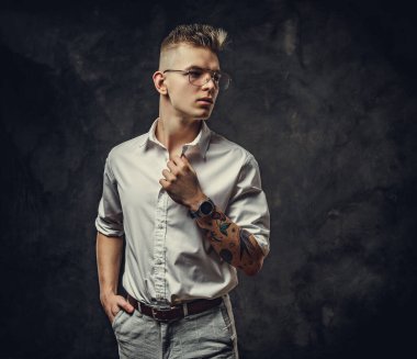 Hippi görünümlü genç bir erkek stüdyoda poz veriyor, gri bir arka planda izole edilmiş.