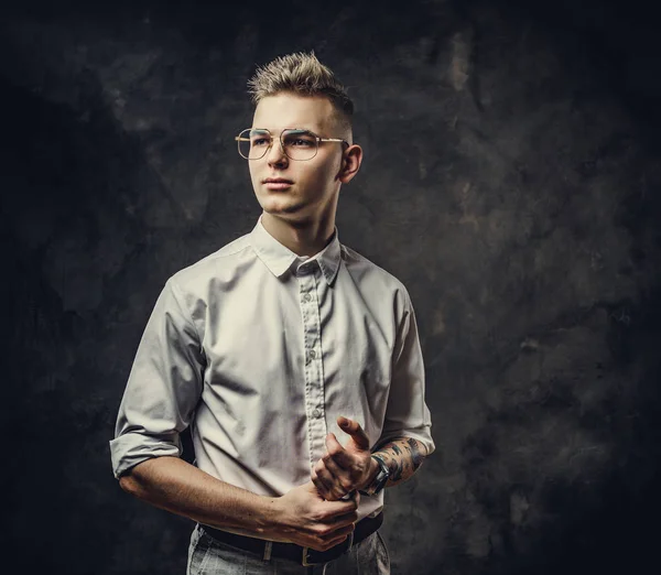 Hippi görünümlü genç bir erkek stüdyoda poz veriyor, sakin görünüyor, gri bir arka planda soyutlanmış.