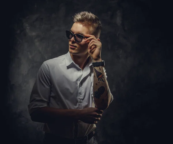 Cool tattoed jonge man op zoek zelfverzekerd en poseren geïsoleerd in een donkere studio in de voorkant van de grijze achtergrond — Stockfoto