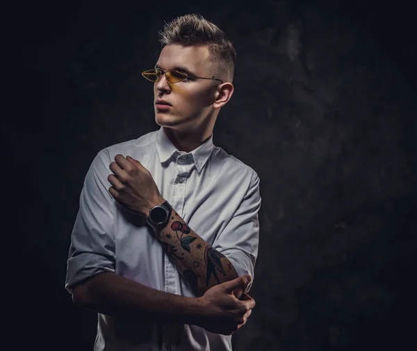 Cool tattoed young male looking confident and posing isolated in a dark studio in front of the grey background