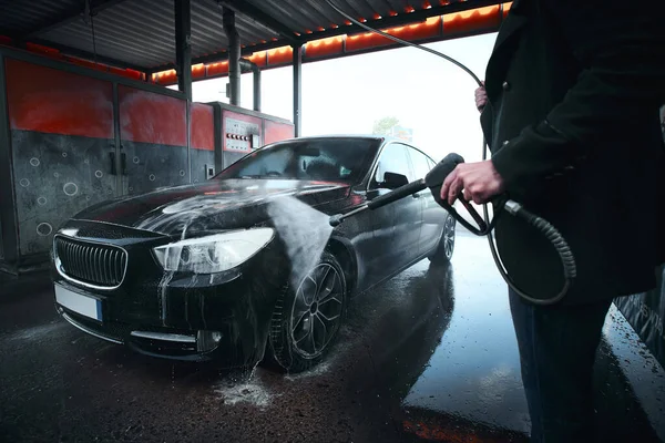 Hands of a serviceman washing car outdoors in a carwash under high pressured water — 스톡 사진