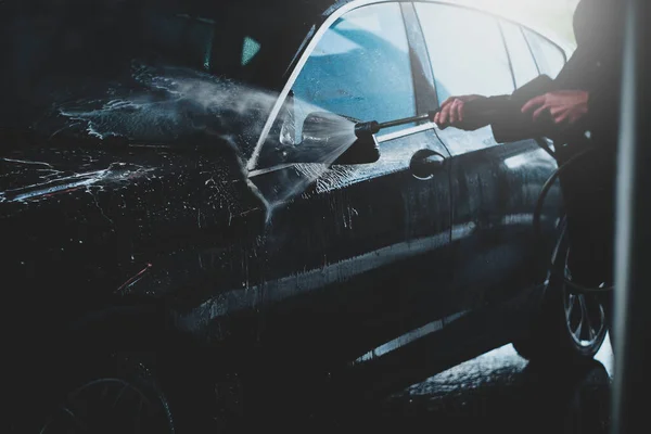 Homem adulto lavando seu carro ao ar livre em uma lavagem de carros sob alta pressão de água — Fotografia de Stock