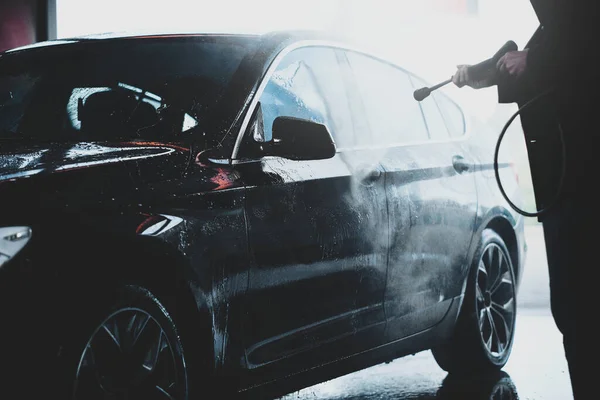 Силует дорослого чоловіка, що миє машину на відкритому повітрі в автомийці під високим тиском води — стокове фото