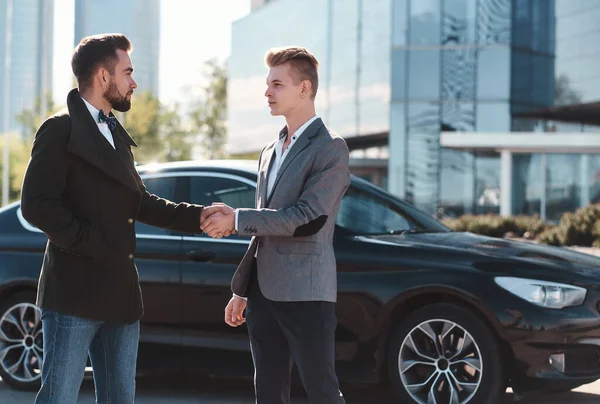 Dva pohlední podnikatelé třesoucí se ruce před černým autem stojící venku — Stock fotografie