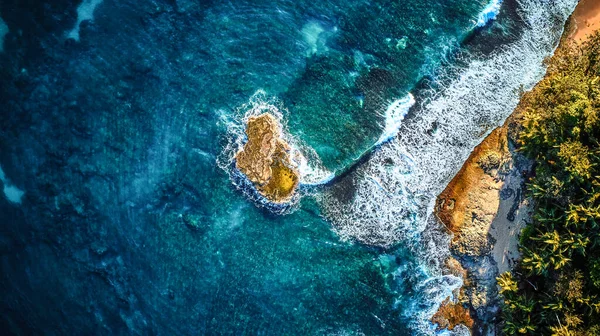 透き通った青い海に囲まれた白い砂の小さな岩の島の近くの日当たりの良いビーチの明るい空中ショット. — ストック写真