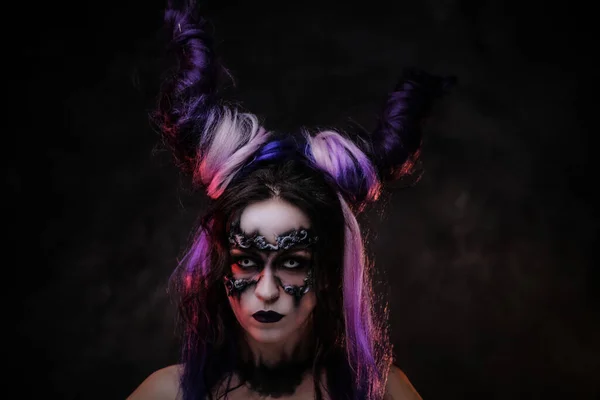 Mujer joven con espeluznante maquillaje oscuro y cuernos violetas posando en un estudio — Foto de Stock