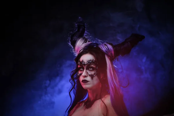 Девушка-косплеер с темным демоническим макияжем и рогами позирует в студии на темном фоне — стоковое фото