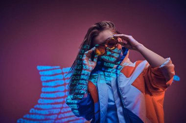Metin projeksiyonu üzerinden canlı bir neon stüdyosunda poz veren dövmeli genç bir siber punk kadının portresi.