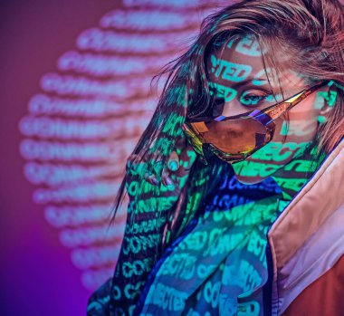 Metin projeksiyonu üzerinden canlı bir neon stüdyoda poz veren dövmeli genç bir yarışçının portresi.
