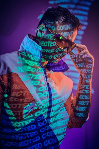 Detailní portrét dospělého tetovaného závodníka pózujícího v živém neonovém studiu nad textovou projekcí — Stock fotografie