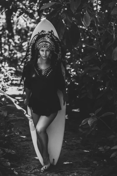 Black and white photo of a semi-nude female posing in the woods with surfing board, aztec conceptual look — Stock Photo, Image