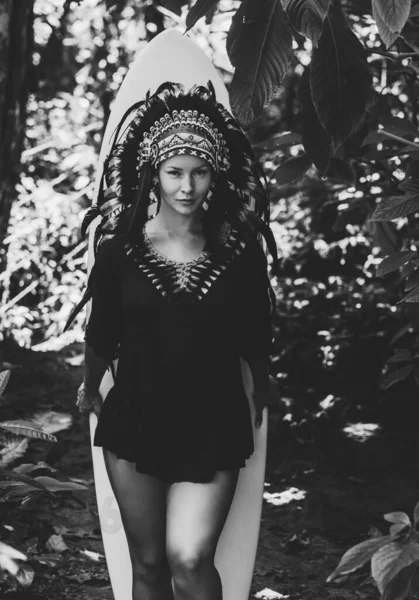 Schwarz-Weiß-Foto einer halbnackten Frau, die im Wald mit Surfbrett posiert, Aztec-Look — Stockfoto