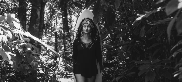 Attraktive Frau posiert im Wald mit Surfbrett und Maya-Indianer-Kopfbedeckung. Schwarz-Weiß-Foto. — Stockfoto