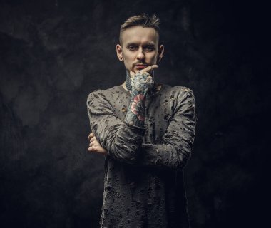 Koyu gri arka planda uzun kollu yırtık kazak giyen dövmeli erkek model.