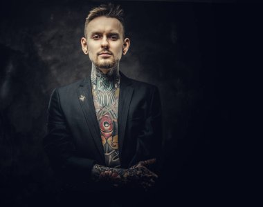 Havalı dövme sanatçısı erkek model. Karanlık bir stüdyoda yarı çıplak dövmeli ve smokinli poz veriyor.