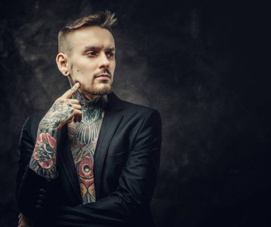 Havalı dövme sanatçısı erkek model. Karanlık bir stüdyoda yarı çıplak dövmeli ve smokinli poz veriyor.