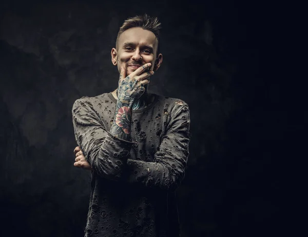 Hombre adulto joven tintado usando jersey rasgado posando en un estudio oscuro sobre un fondo gris —  Fotos de Stock