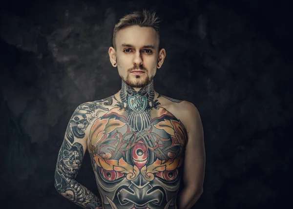 Inked male model posing in a dark studio with grey background with half-naked tattooed body.