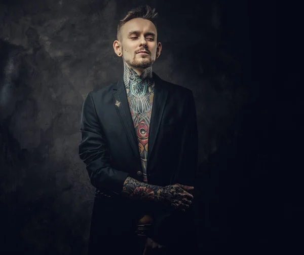 Sebevědomý a potetovaný tetovaný mužský model pózující v tmavém ateliéru s polonahým tetovaným tělem a smokingem — Stock fotografie