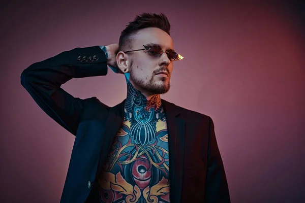 Tatuaje modelo masculino posando en un estudio de neón con cuerpo tatuado semidesnudo, esmoquin y gafas de sol. Retrato vertical —  Fotos de Stock