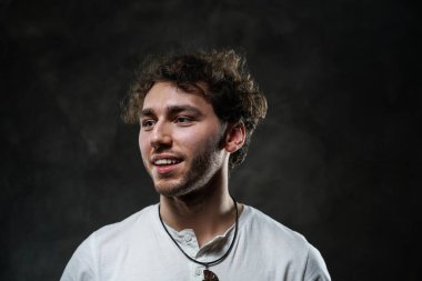 Karanlık bir stüdyoda sıradan giysiler içinde gülümseyen çekici bir erkek model.
