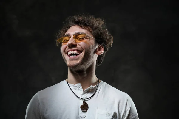 Glada och lockiga man bär solglasögon poserar i den mörka studion — Stockfoto