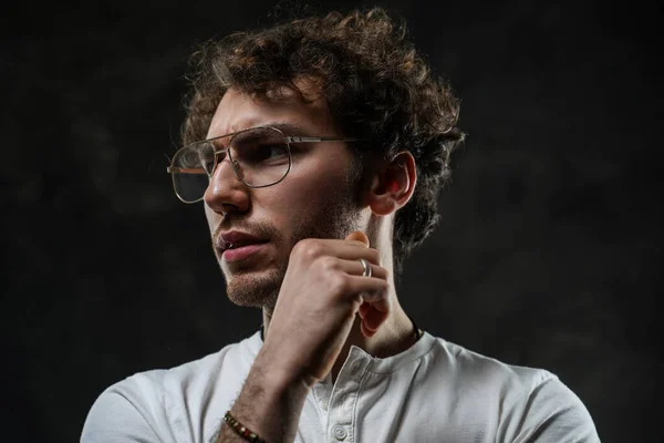 Portrait of a handsome casual guy with curly hair posing in the dark studio — Stock Photo, Image
