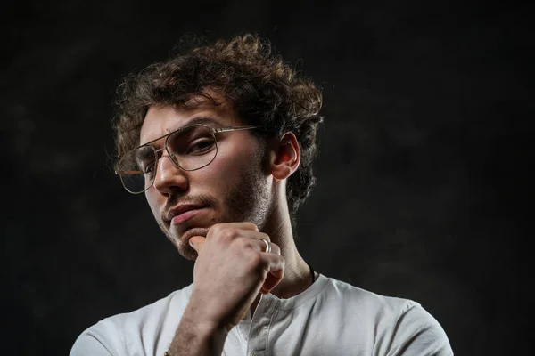 Portrait of a handsome casual guy with curly hair posing in the dark studio — Stock Photo, Image