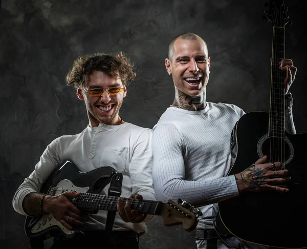 Retrato de dos músicos guapos con camisas blancas posando en el oscuro estudio con instrumentos musicales — Foto de Stock