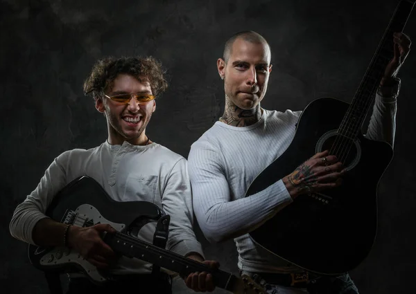 スタジオでポーズをとりながらカジュアルな服を着た笑顔のギタリスト2人のギターを持った写真家 — ストック写真