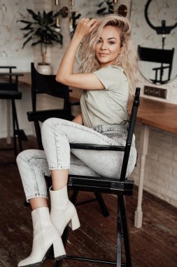 Uzun bir sandalyede parlak bir odada oturan kıvırcık saçlı şehvetli ve çekici bir genç kadın.