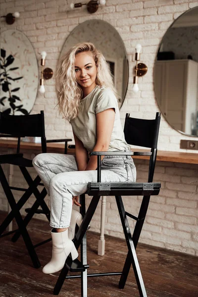 Mulher branca bonito e bonito com cabelo encaracolado sentado em uma cadeira de maquiagem no estúdio — Fotografia de Stock