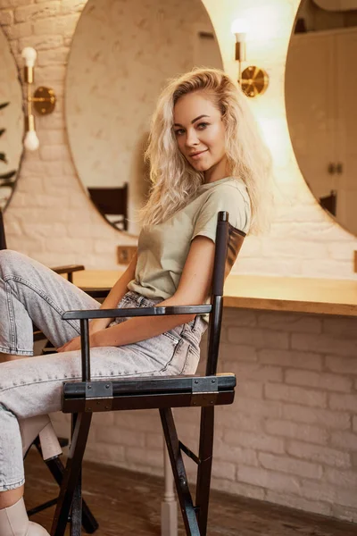 Linda y hermosa mujer caucásica con el pelo rizado sentado en una silla de maquillaje en el estudio — Foto de Stock