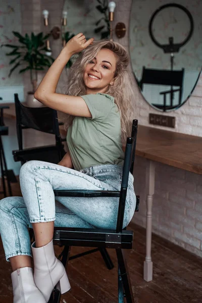 Linda y hermosa mujer caucásica con el pelo rizado sentado en una silla de maquillaje en el estudio — Foto de Stock