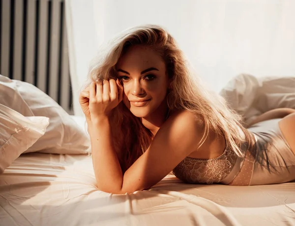 Entzückende Frau zeigt ihren Körper in Spitzenunterwäsche zwischen Bettlaken — Stockfoto