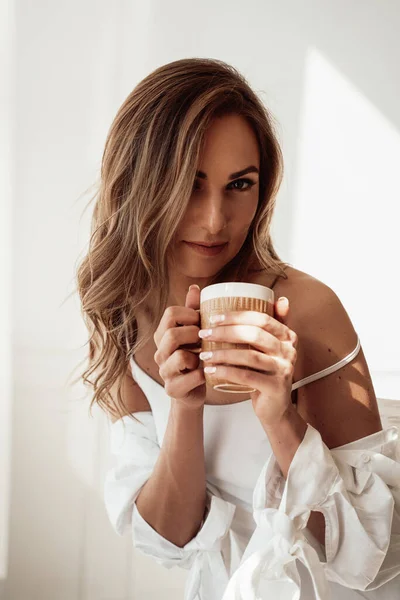 Красива молода жінка в нижній білизні позує з чашкою кави на білому тлі — стокове фото