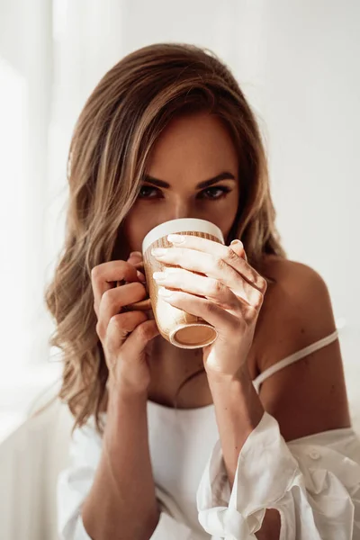 İç çamaşırlı zarif genç bayan beyaz arka planda bir fincan kahve yudumluyor. — Stok fotoğraf