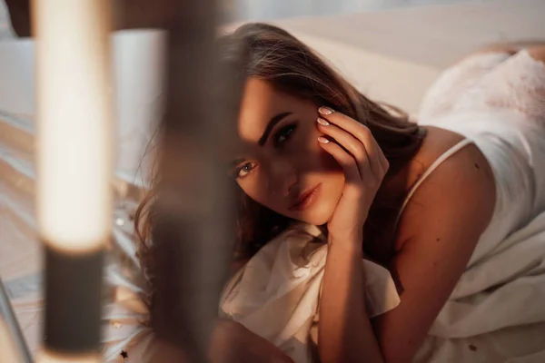 Retrato de uma jovem e bela mulher semi-nua em lingerie de renda branca que coloca em uma cama acolhedora — Fotografia de Stock
