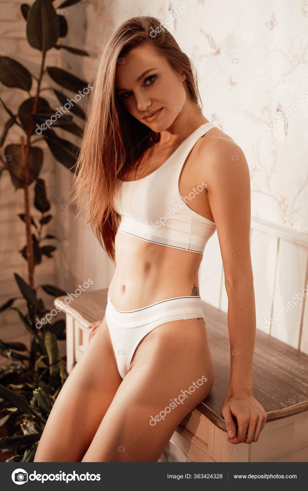 Young female model in sporty underwear sitting on the floor in a room  filled with sunlight Stock Photo by fxquadro